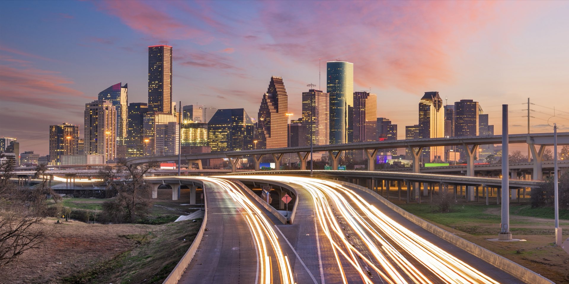 The Houston skyline at dusk, with traffic light trails on the freeway.